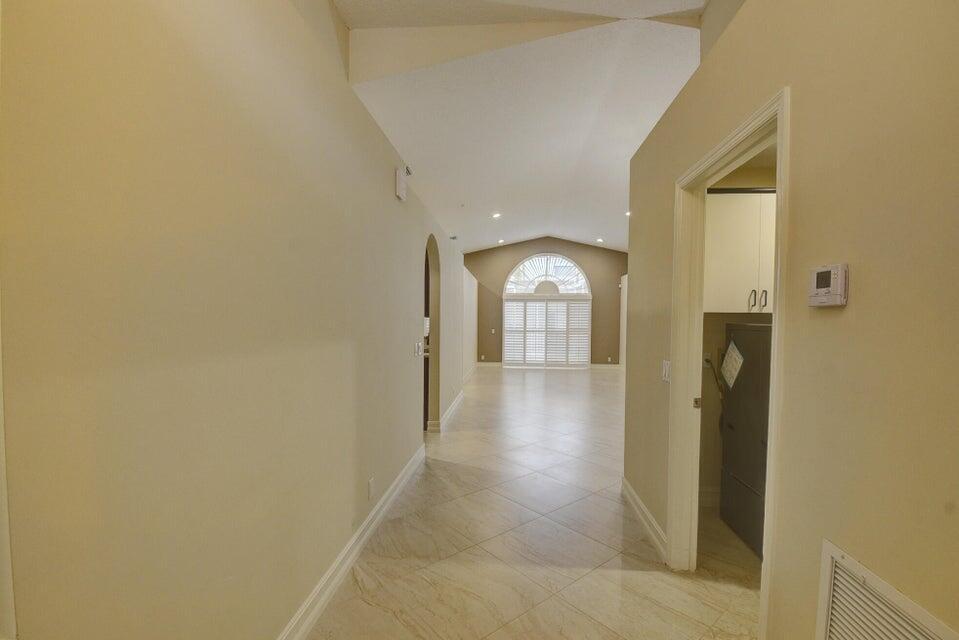 A hallway with light-colored tile flooring leads toward a bright living area with vaulted ceilings — 18967 Treble Lane, Boca Raton FL 33498, BOCA RATON, FL