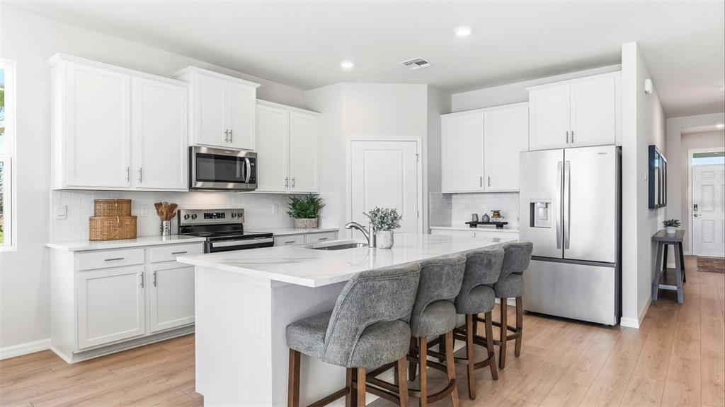 A modern kitchen features white cabinets, stainless steel appliances, a marble-topped island, and gray stools — 17305 SALTBUSH TRAIL, PARRISH, FL