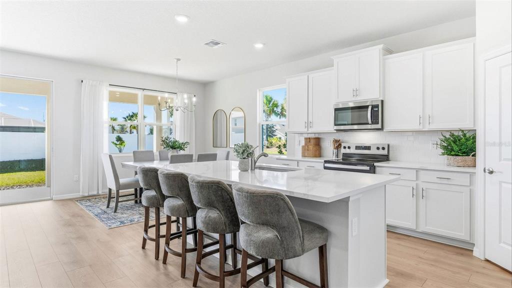 A bright kitchen features white cabinetry, a large quartz island, and an adjacent dining area — 17305 SALTBUSH TRAIL, PARRISH, FL