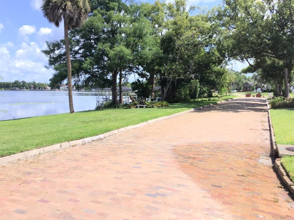 A brick-paved road runs alongside a grassy lawn bordering a lake with mature trees — 120 BROADVIEW AVENUE, WINTER PARK, FL
