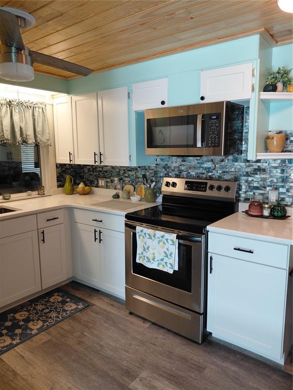 A kitchen features white cabinets, stainless steel appliances, a blue tiled backsplash, and wood ceilings — 1451 BLUE HERON DRIVE, ENGLEWOOD, FL