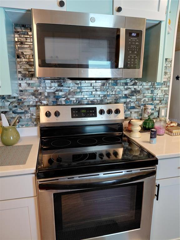 A stainless steel microwave and electric range are set against a blue-toned mosaic tile backsplash — 1451 BLUE HERON DRIVE, ENGLEWOOD, FL