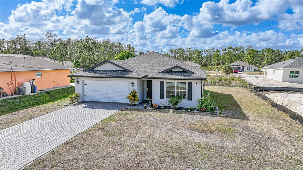 A single-story house with a white stucco exterior, a gray shingled roof, and a paver driveway — 1923 KESTER AVENUE, LEHIGH ACRES, FL