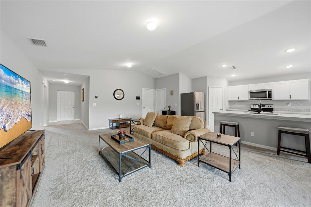 A living room with carpeted floors, a tan sofa, and an open kitchen with white cabinets — 1923 KESTER AVENUE, LEHIGH ACRES, FL