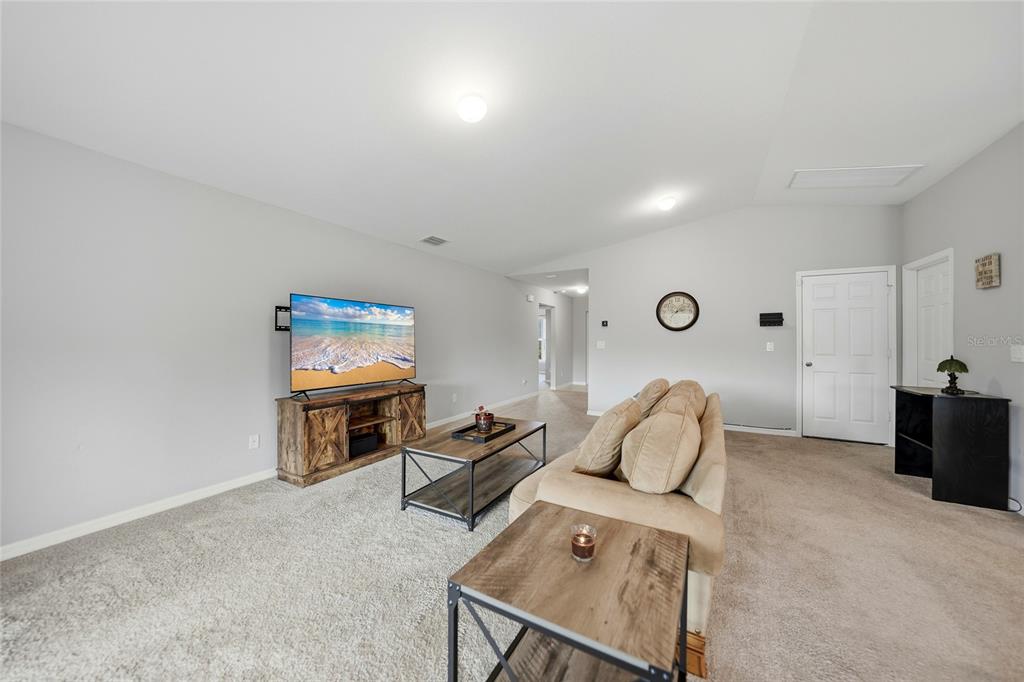 A living room features gray carpet, light gray walls, a television on a wooden stand, and a sofa — 1923 KESTER AVENUE, LEHIGH ACRES, FL