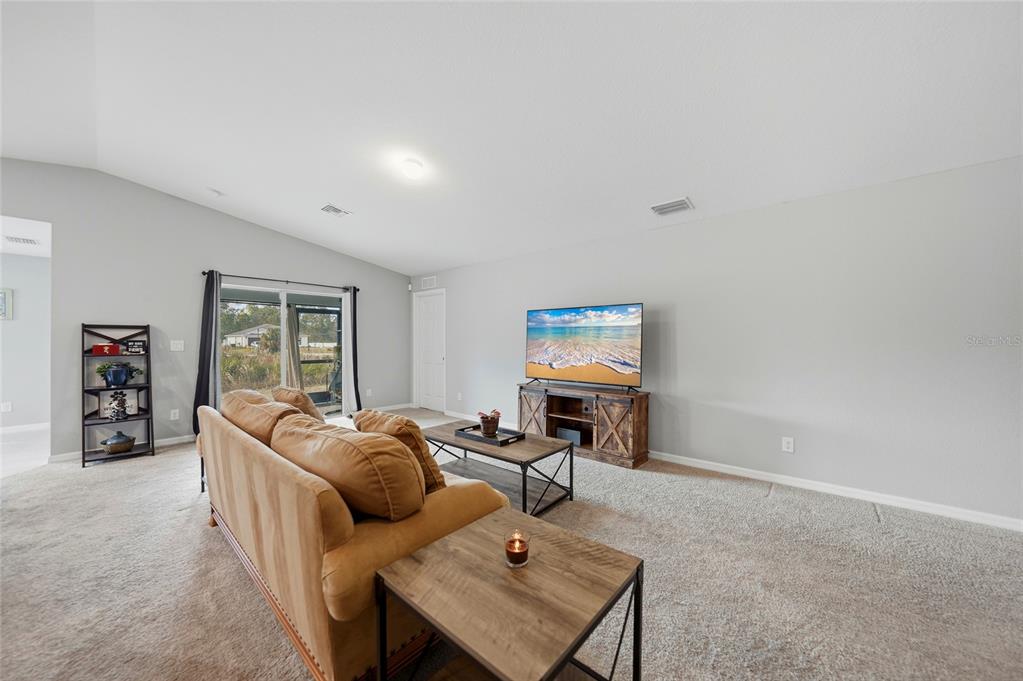 A living room features a tan sofa, a wooden media console, and a sliding glass door — 1923 KESTER AVENUE, LEHIGH ACRES, FL