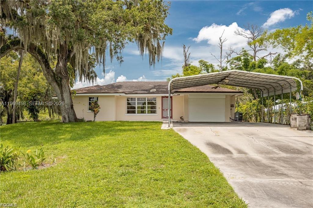A single-story house with a metal carport and a large tree in the front yard — 2030 Ft Denaud Rd, La Belle FL 33935, LA BELLE, FL
