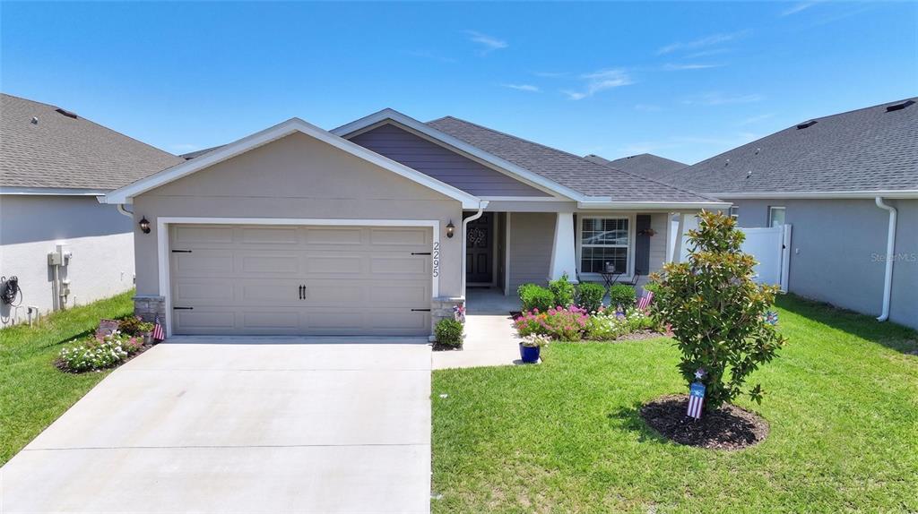 A single-story suburban house features a two-car garage, a front porch, and a landscaped yard — 2295 SUNSET WAY, DAVENPORT, FL
