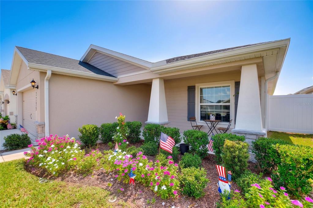 A tan single-story house exterior features a covered front porch, landscaping, and American flag decorations — 2295 SUNSET WAY, DAVENPORT, FL