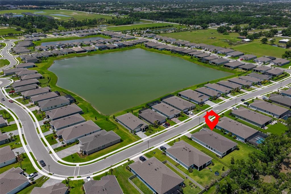 An aerial view shows a suburban neighborhood with houses surrounding a large central pond — 12342 54TH STREET E, PARRISH, FL