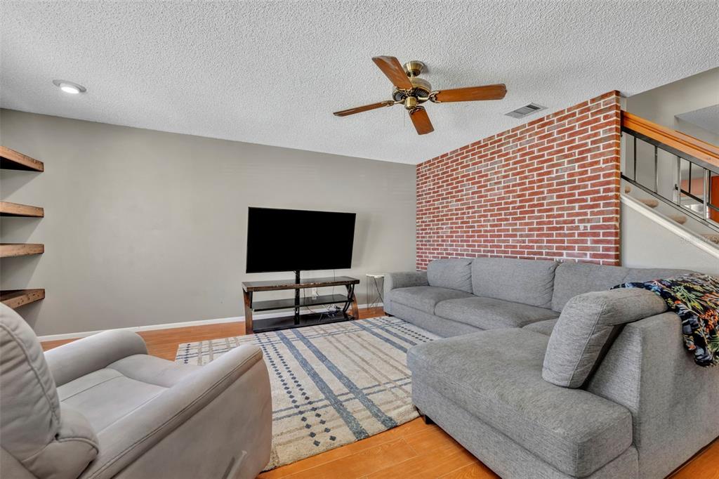A living room features a brick accent wall, a gray sectional sofa, and a ceiling fan — 2810 CORNERSTONE COURT, APOPKA, FL