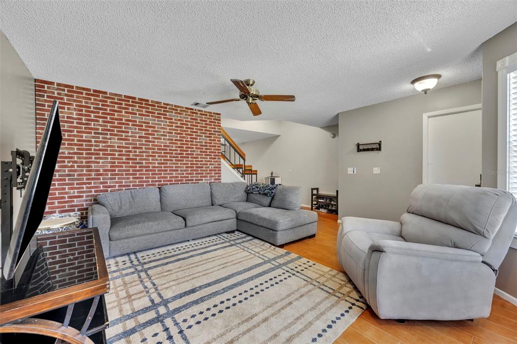 A living room features a brick accent wall, a gray sectional sofa, and a recliner — 2810 CORNERSTONE COURT, APOPKA, FL