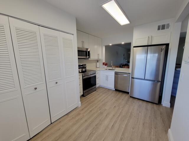 A kitchen with white cabinets, stainless steel appliances, and light wood-look flooring — 6650 S Oriole Boulevard # 4080, Delray Beach FL 33446, DELRAY BEACH, FL