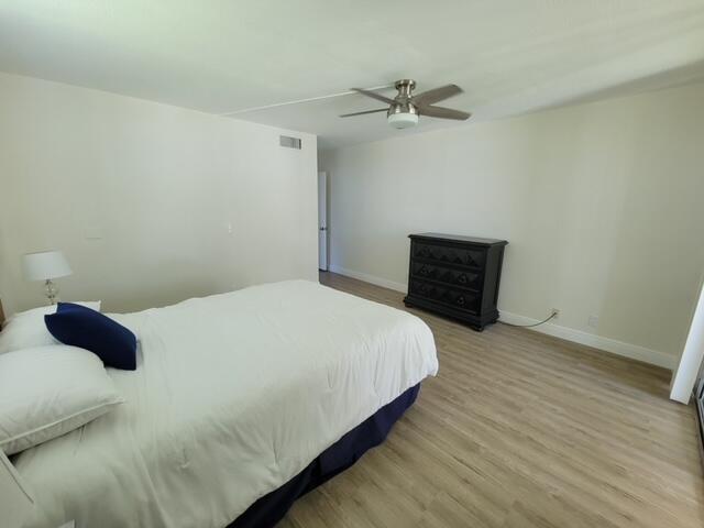 A bedroom with light-colored walls, wood-look flooring, a ceiling fan, and a black dresser — 6650 S Oriole Boulevard # 4080, Delray Beach FL 33446, DELRAY BEACH, FL