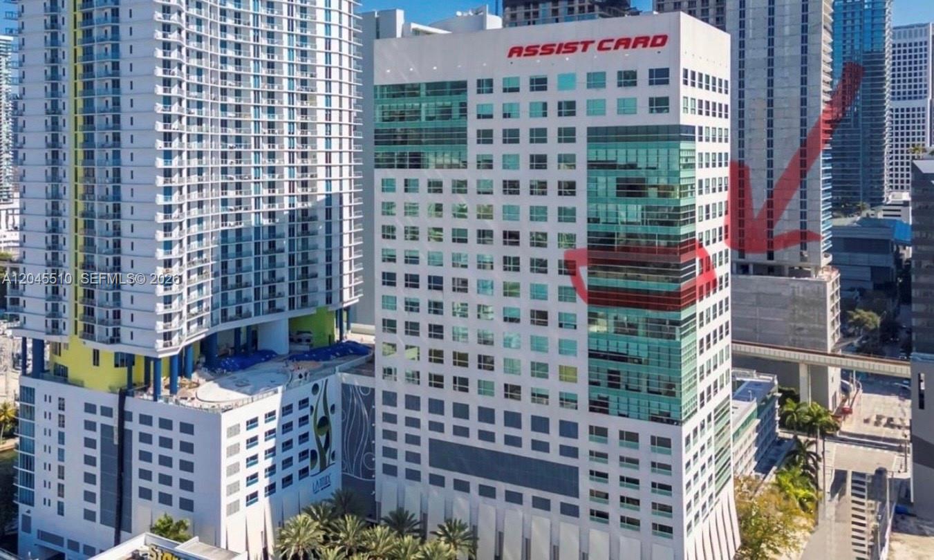 An exterior view of a tall office building with an Assist Card sign on top — 175 SW 7th St # 1212, Miami FL 33130, MIAMI, FL