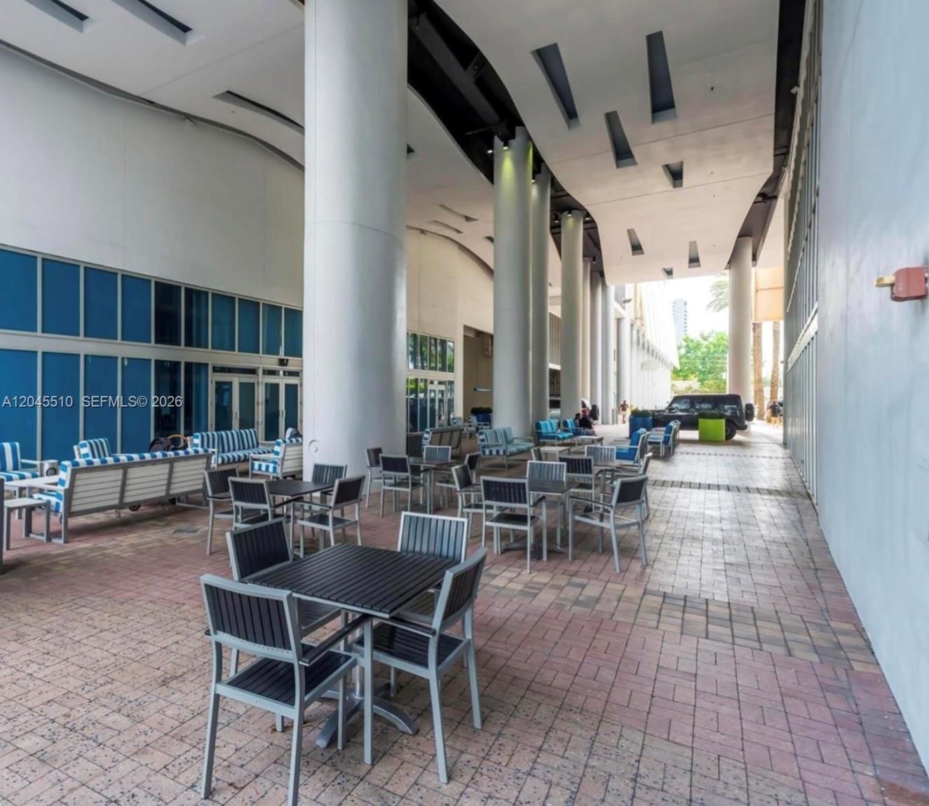 An outdoor patio area features multiple tables and chairs under a large modern architectural overhang — 175 SW 7th St # 1212, Miami FL 33130, MIAMI, FL