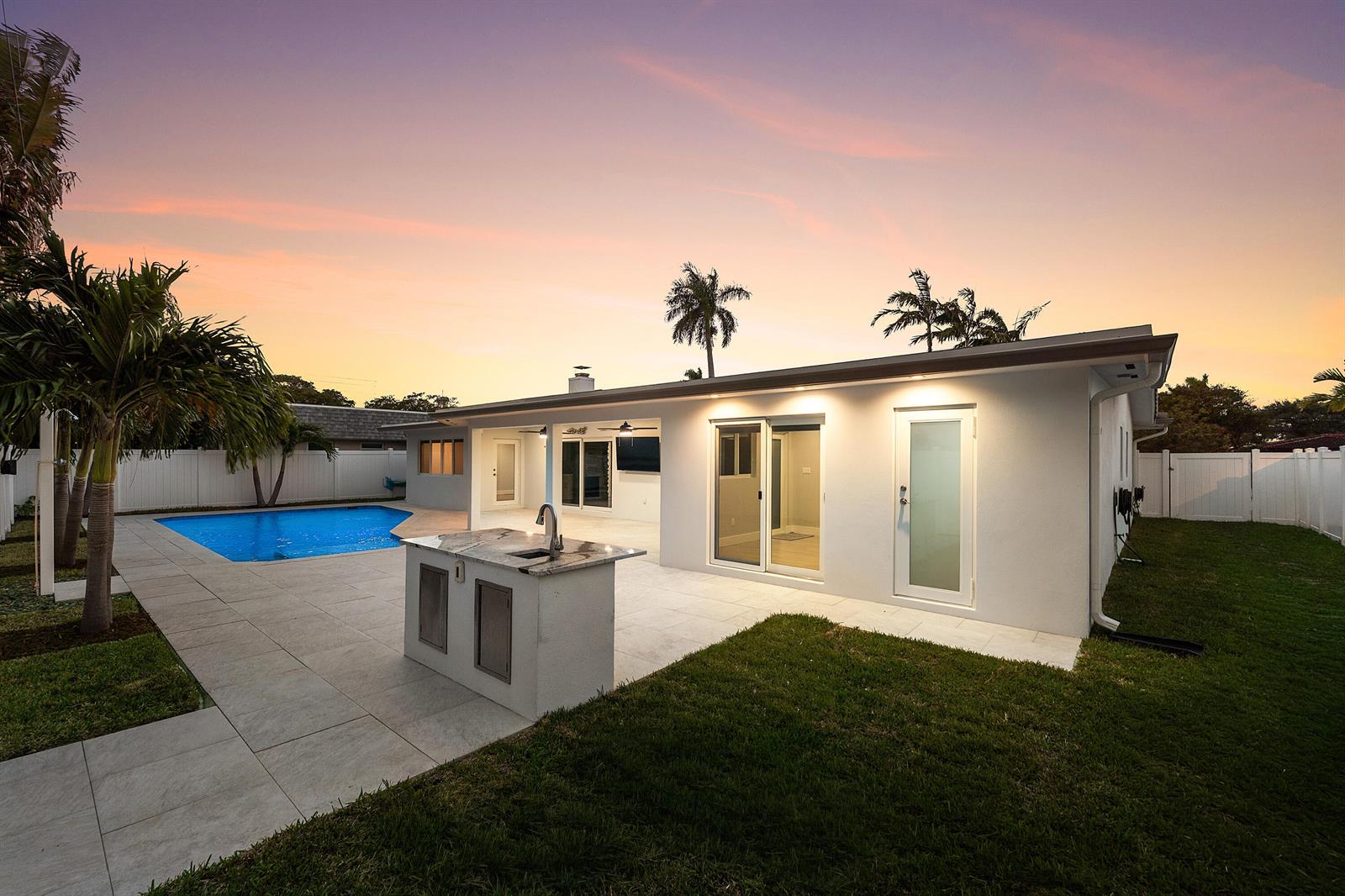 A backyard features a white house with a patio, outdoor kitchen, and swimming pool — 2846 NE 35th Court, Lighthouse Point FL 33064, LIGHTHOUSE POINT, FL