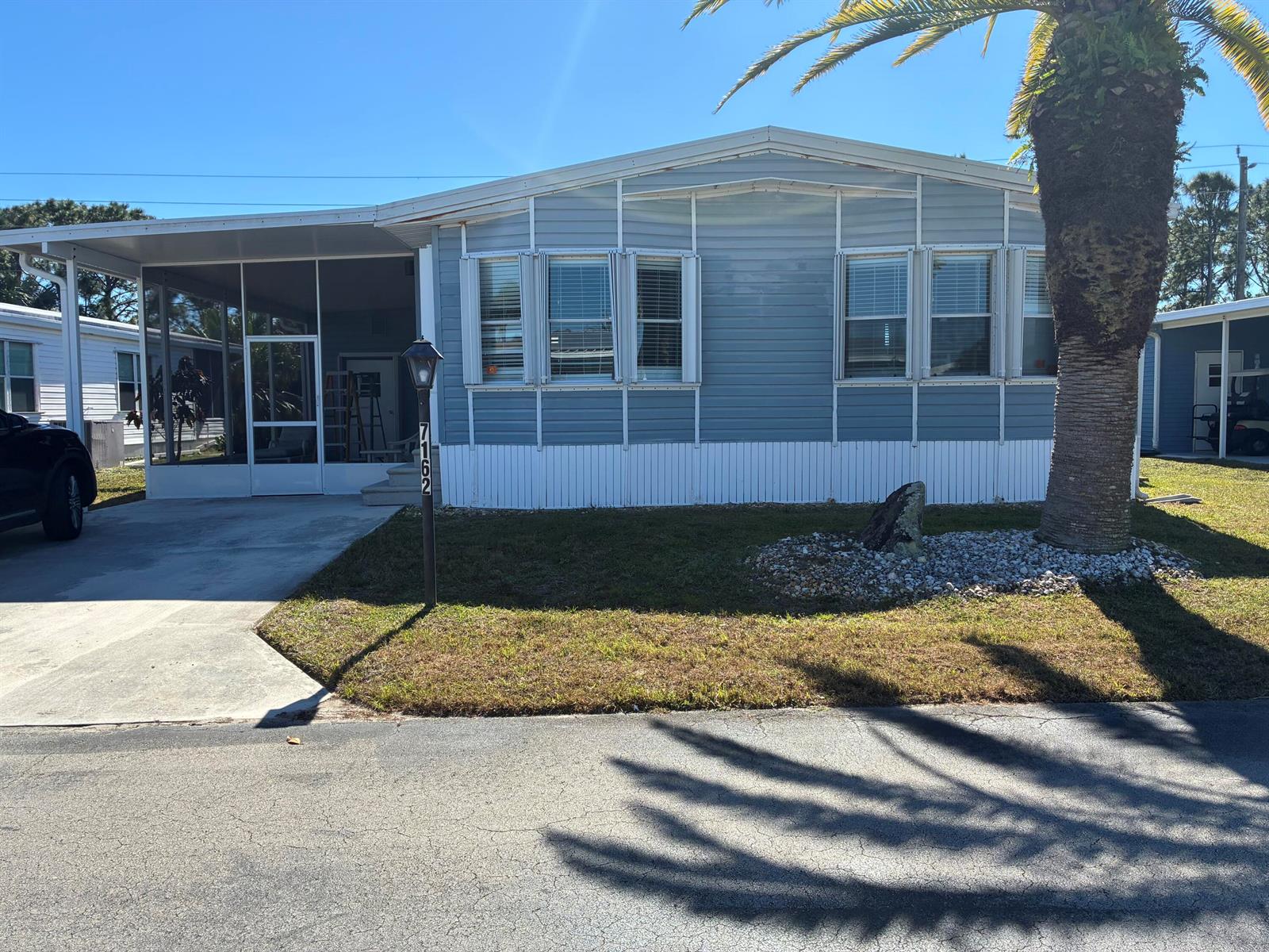 A light blue manufactured home with a screened-in porch, driveway, and a large palm tree — 7162 SE Sweetwood Terrace, Stuart FL 34997, STUART, FL