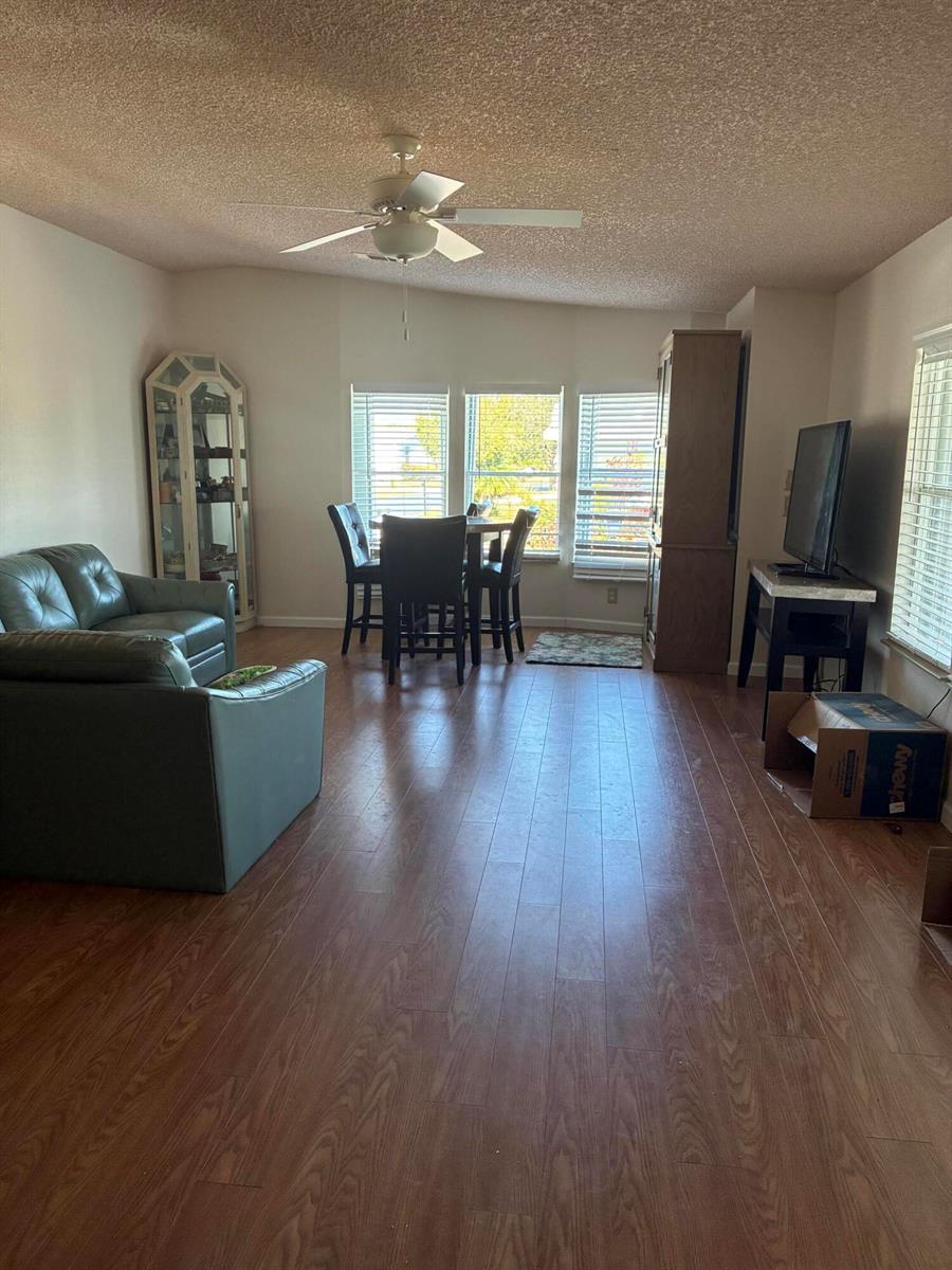 A living and dining area features wood-look flooring, a ceiling fan, and large windows — 7162 SE Sweetwood Terrace, Stuart FL 34997, STUART, FL