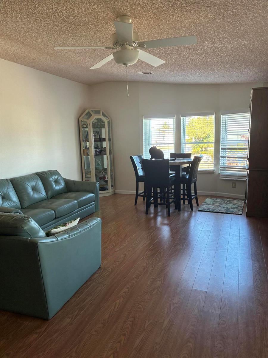 A living and dining area with wood-look flooring, a ceiling fan, and a corner curio cabinet — 7162 SE Sweetwood Terrace, Stuart FL 34997, STUART, FL