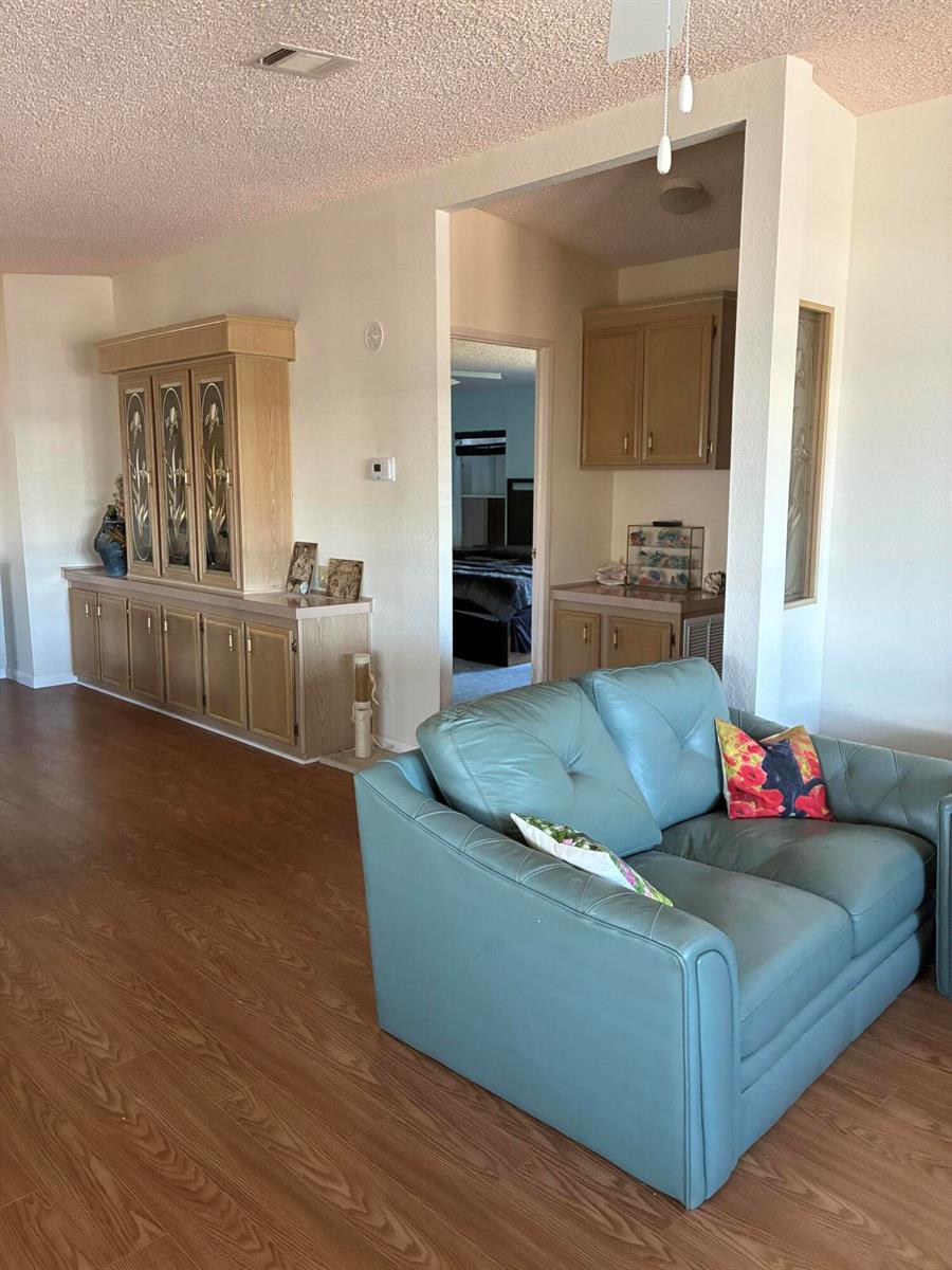 A living room features light wood cabinetry, a teal leather loveseat, and wood-look flooring — 7162 SE Sweetwood Terrace, Stuart FL 34997, STUART, FL