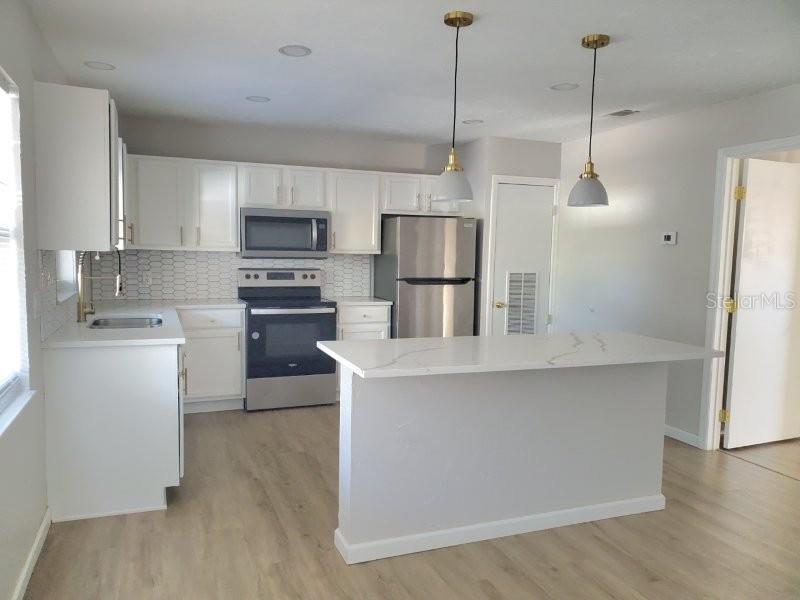 A kitchen features white cabinets, stainless steel appliances, a center island, and light wood flooring — 4390 SIBLEY BAY STREET UNIT J-D, PUNTA GORDA, FL