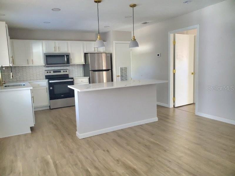 A modern kitchen features white cabinets, stainless steel appliances, and a central island — 4390 SIBLEY BAY STREET UNIT J-D, PUNTA GORDA, FL