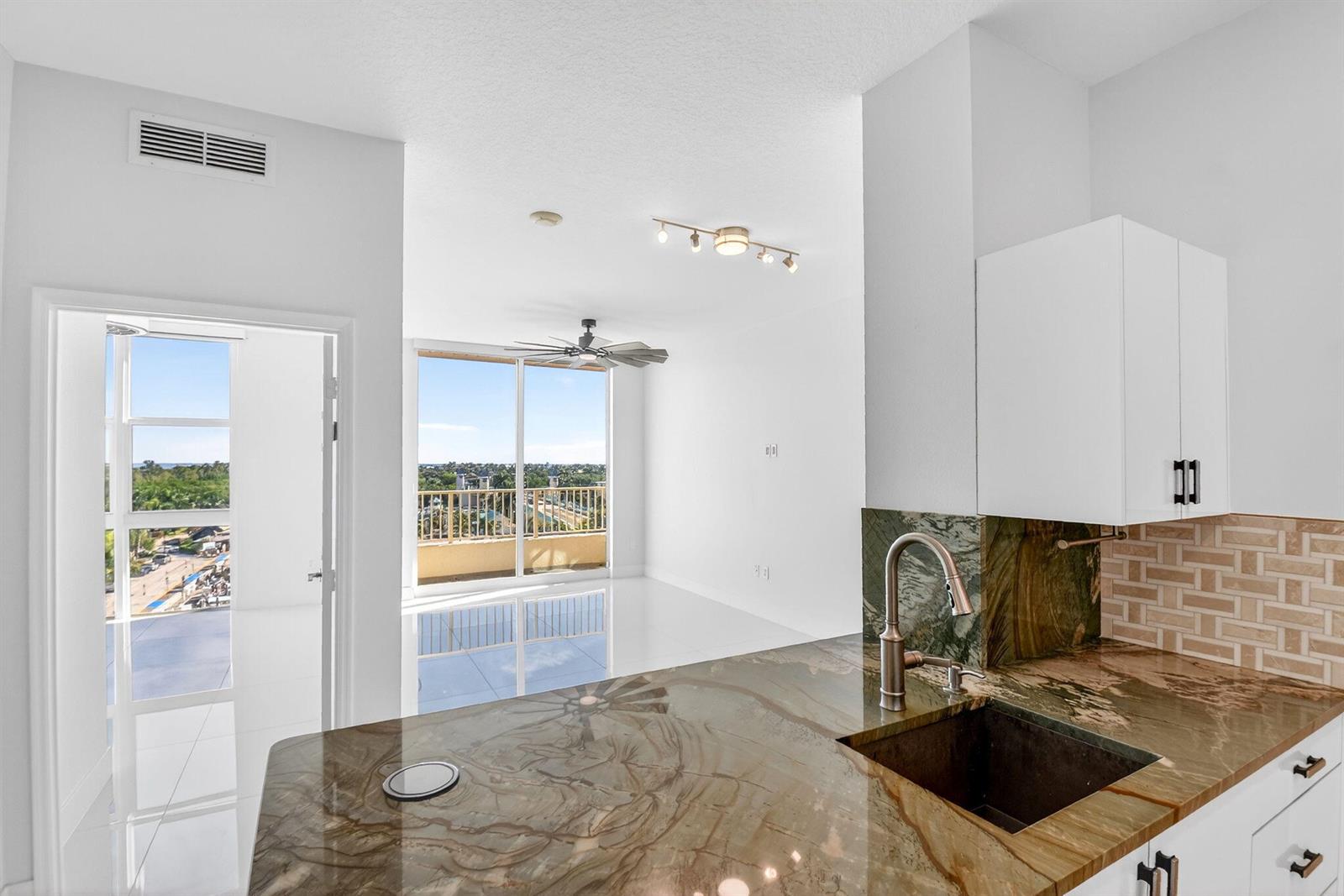 A kitchen with stone countertops and a sink overlooks a bright living area with balcony — 100 NE 6th Street # 704, Boynton Beach FL 33435, BOYNTON BEACH, FL