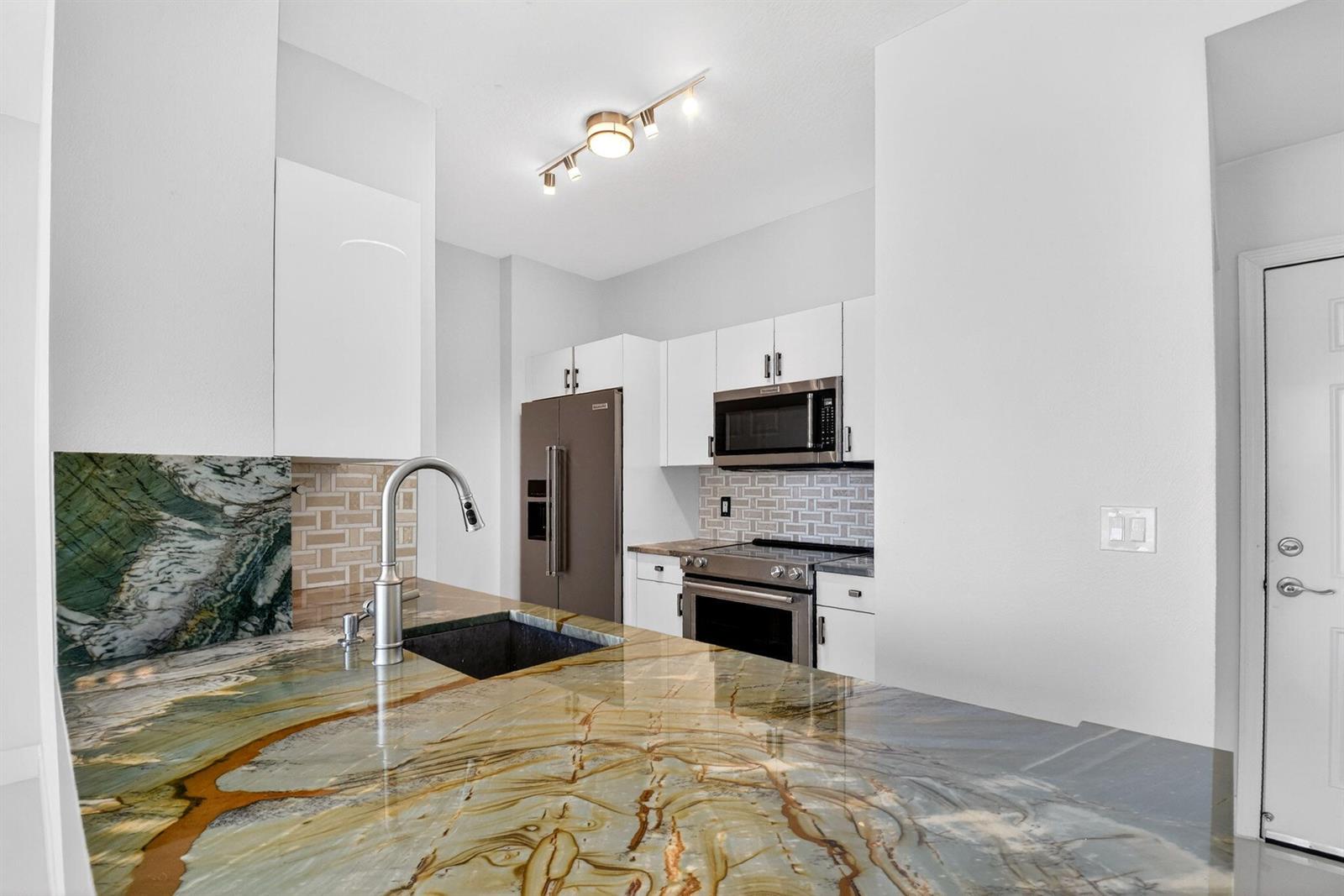 A kitchen features a large, patterned stone countertop, white cabinets, and stainless steel appliances — 100 NE 6th Street # 704, Boynton Beach FL 33435, BOYNTON BEACH, FL