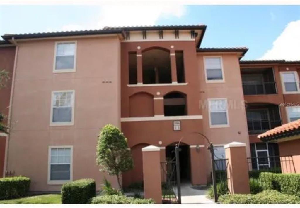 A three-story apartment building exterior with a central arched entryway and tan stucco walls — 5566 METROWEST BOULEVARD UNIT 301, ORLANDO, FL