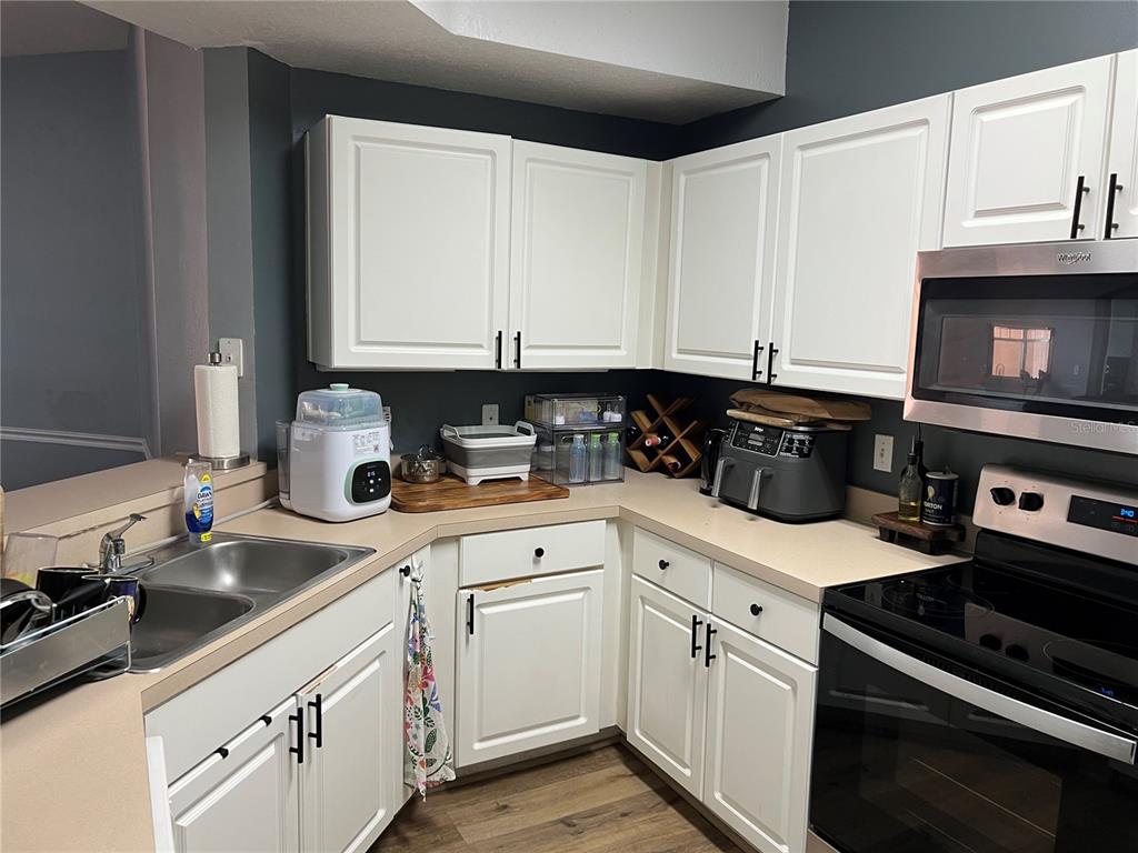 A kitchen features white cabinets, dark gray walls, a stainless steel microwave, and beige countertops — 5566 METROWEST BOULEVARD UNIT 301, ORLANDO, FL