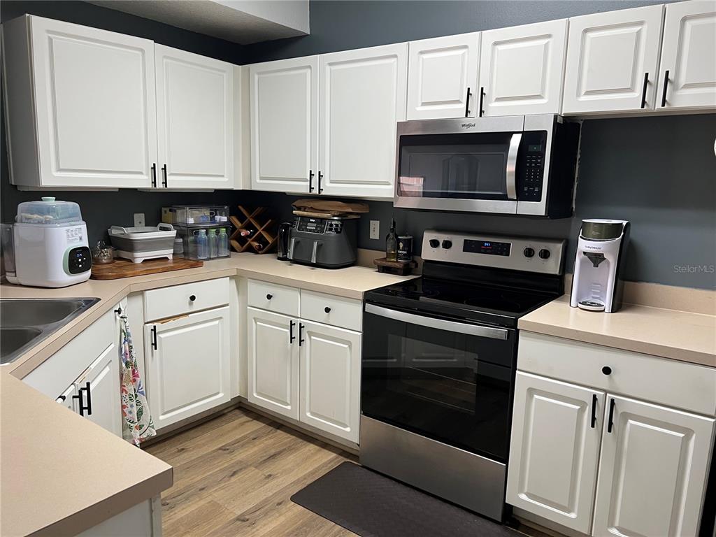 A kitchen features white cabinets, stainless steel appliances, and dark gray walls — 5566 METROWEST BOULEVARD UNIT 301, ORLANDO, FL
