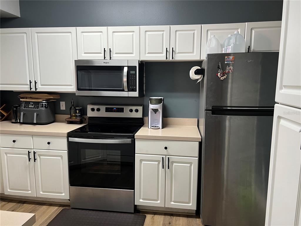 A kitchen features white cabinets, stainless steel appliances, and light-colored countertops against a dark wall — 5566 METROWEST BOULEVARD UNIT 301, ORLANDO, FL