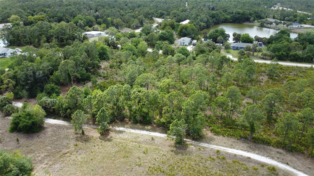 An aerial view shows a wooded lot with a dirt path and nearby residential houses — 27276 DEL RIO DRIVE, PUNTA GORDA, FL