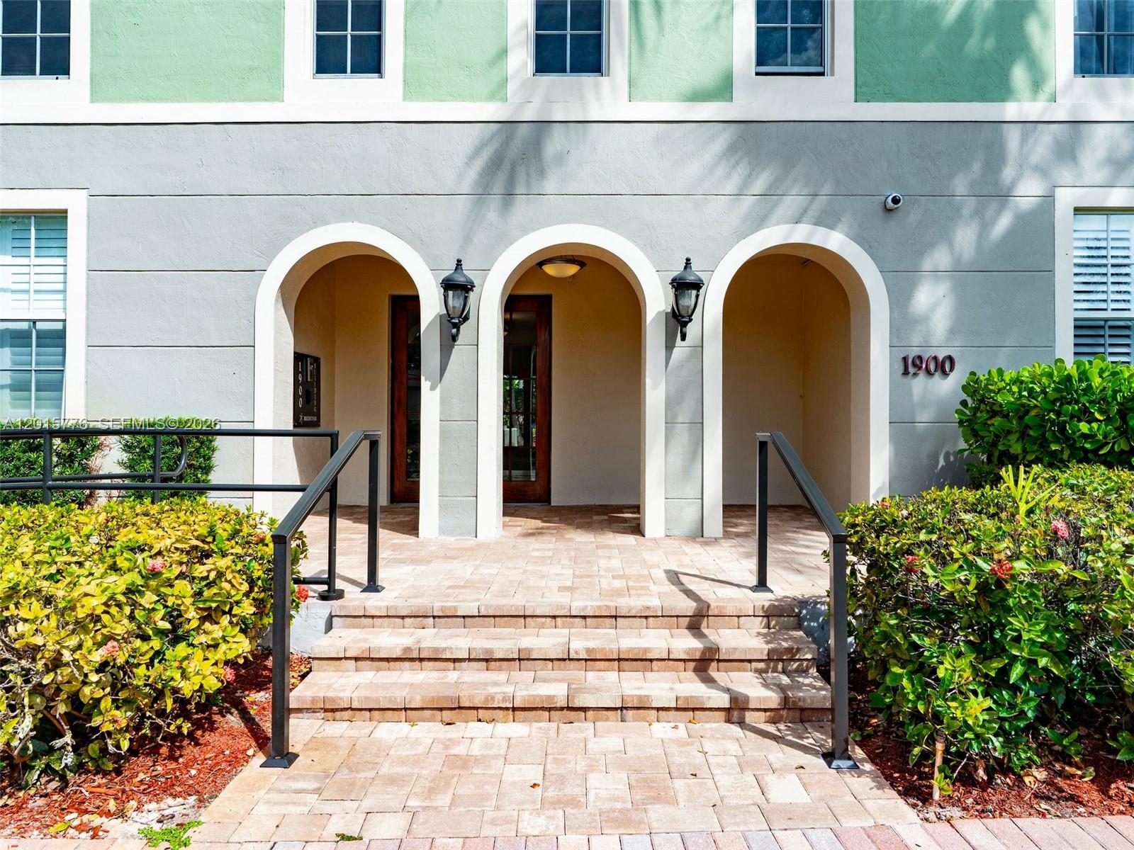 The exterior of a building features three arched entryways with brick steps and railings — 1900 Van Buren St # 112B, Hollywood FL 33020, HOLLYWOOD, FL