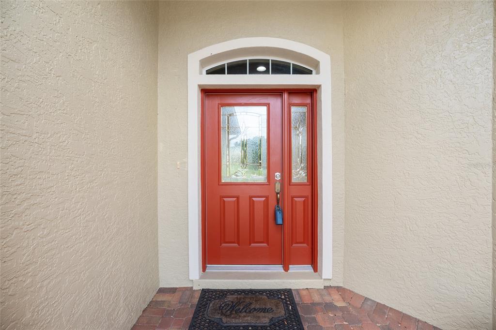 A red front door with a glass insert and sidelight sits within a beige stucco entryway — 9274 SW 94TH LOOP, OCALA, FL