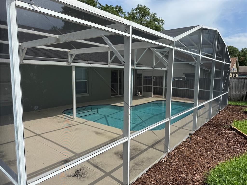 A swimming pool is enclosed by a screened lanai behind a house with a patio — 8843 PARLIAMENT COURT, KISSIMMEE, FL