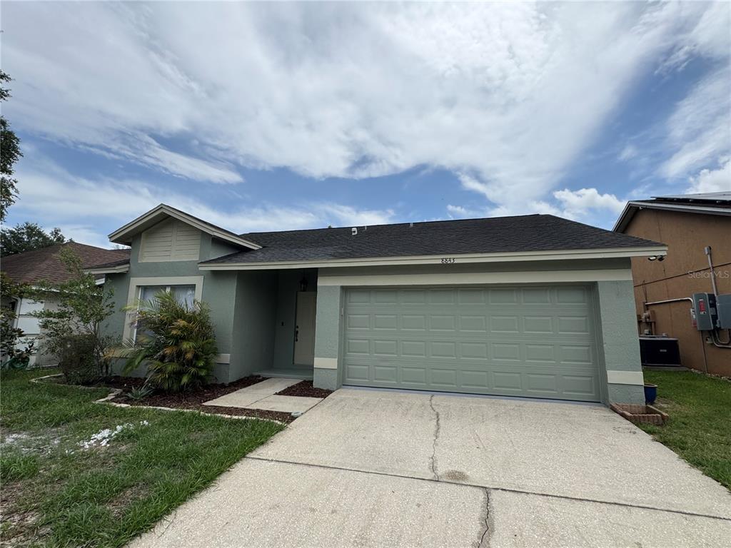A single-story house with a green stucco exterior, a two-car garage, and a concrete driveway — 8843 PARLIAMENT COURT, KISSIMMEE, FL