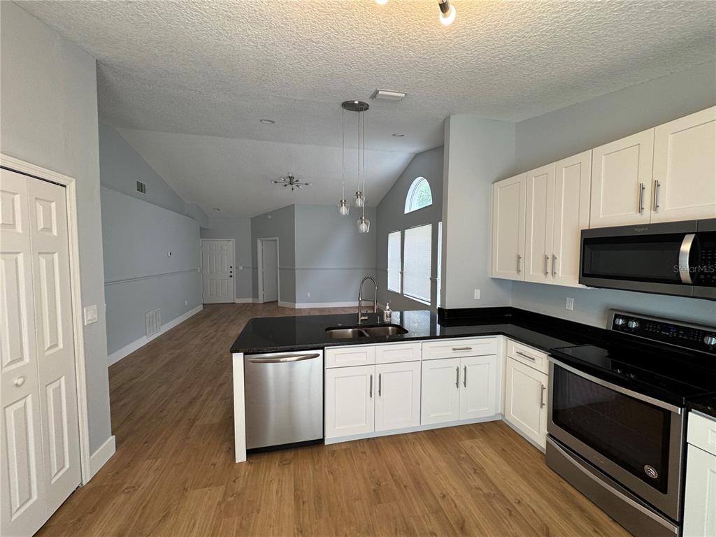 A kitchen with white cabinets, black countertops, and stainless steel appliances opens to a living area — 8843 PARLIAMENT COURT, KISSIMMEE, FL
