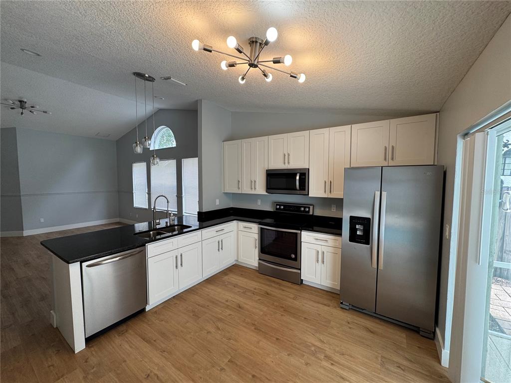 A kitchen features white cabinets, black countertops, stainless steel appliances, and light wood flooring — 8843 PARLIAMENT COURT, KISSIMMEE, FL