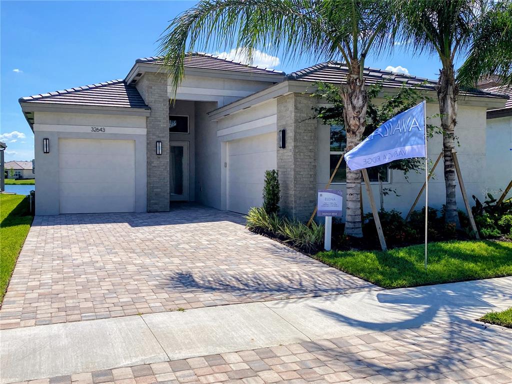 A view of a pond behind a grassy yard with houses in the distance — 32643 NEROLI STREET, WESLEY CHAPEL, FL