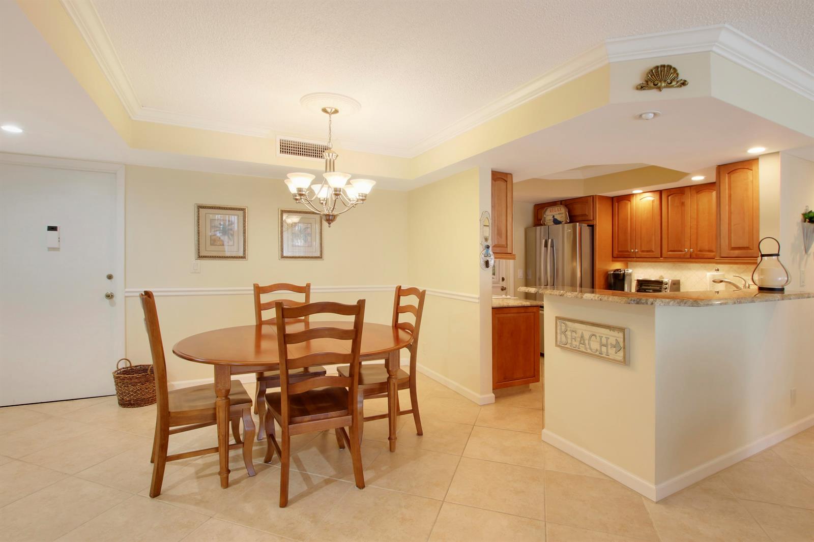 A dining area with a wooden table and chairs adjacent to a kitchen with cabinets — 630 Ocean Drive # 102, Juno Beach FL 33408, JUNO BEACH, FL