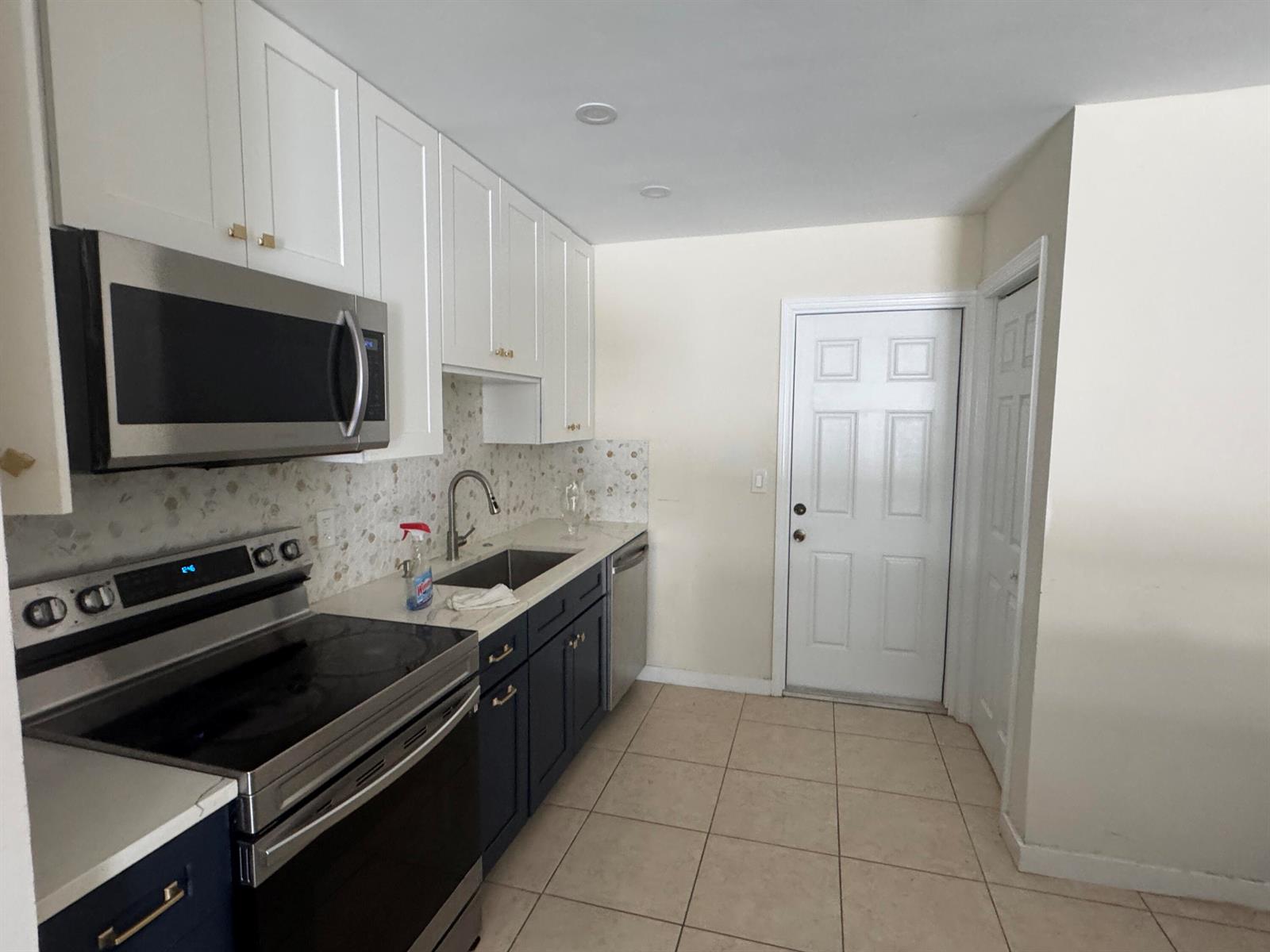 A kitchen features white upper cabinets, dark lower cabinets, stainless steel appliances, and tiled flooring — 1869 Windsor Drive # 1869, North Palm Beach FL 33408, NORTH PALM BEACH, FL