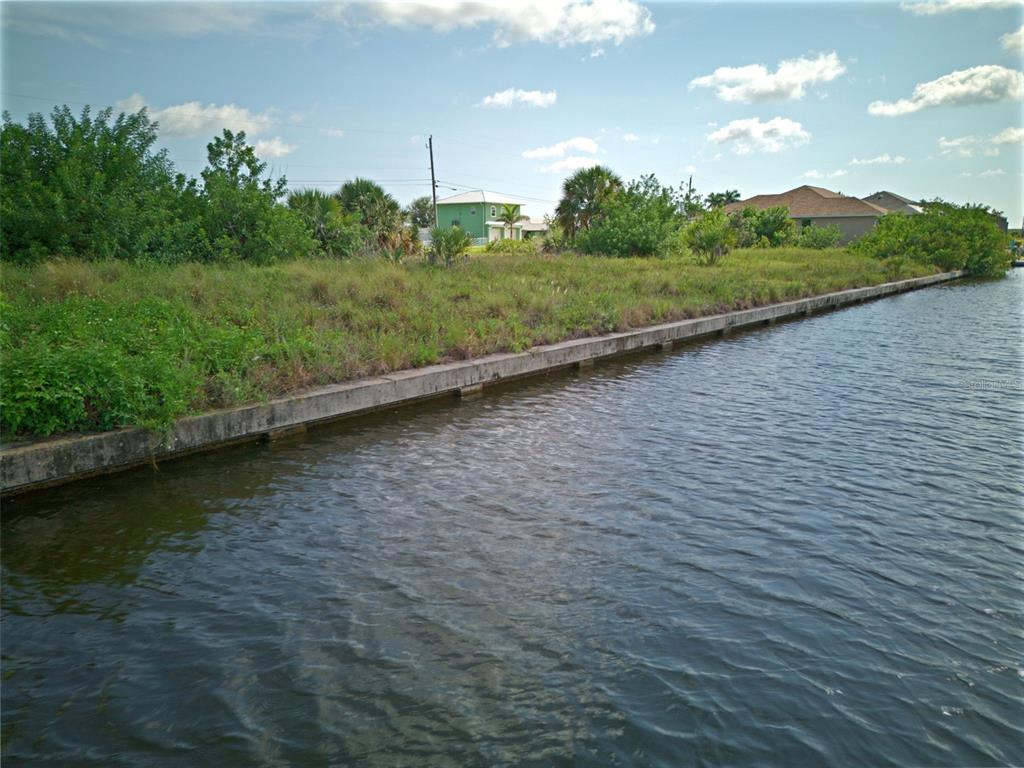 A vacant waterfront lot features a concrete seawall bordering a canal under a blue sky — 15482 MEACHAM CIRCLE, PORT CHARLOTTE, FL