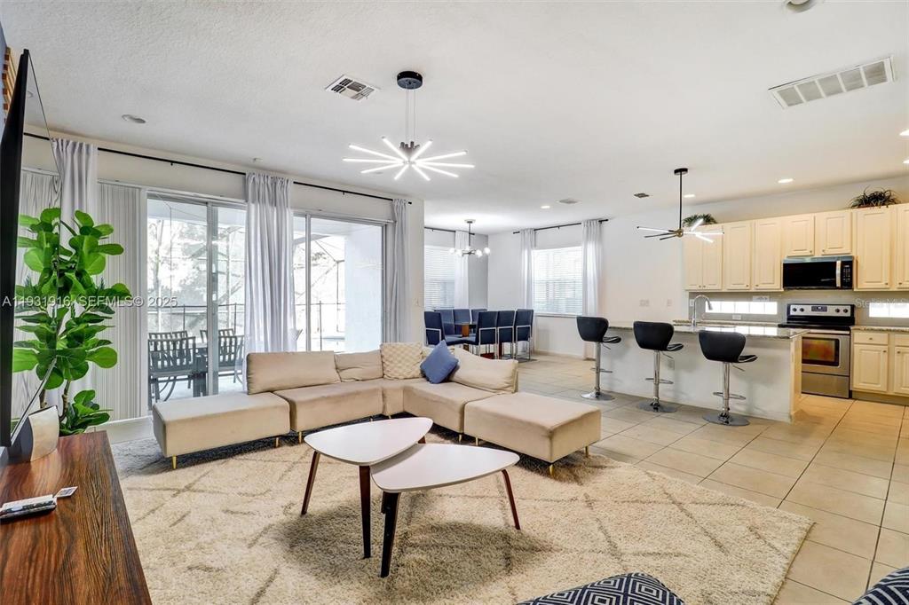An open-concept living room and kitchen feature a beige sectional, tile floors, and modern lighting — 4503 MONADO DRIVE, KISSIMMEE, FL