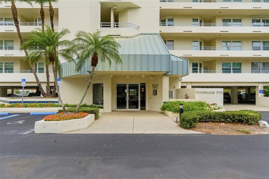 The exterior entrance of a multi-story apartment building features a metal awning and landscaping — 7932 SAILBOAT KEY BOULEVARD S UNIT 701, SOUTH PASADENA, FL