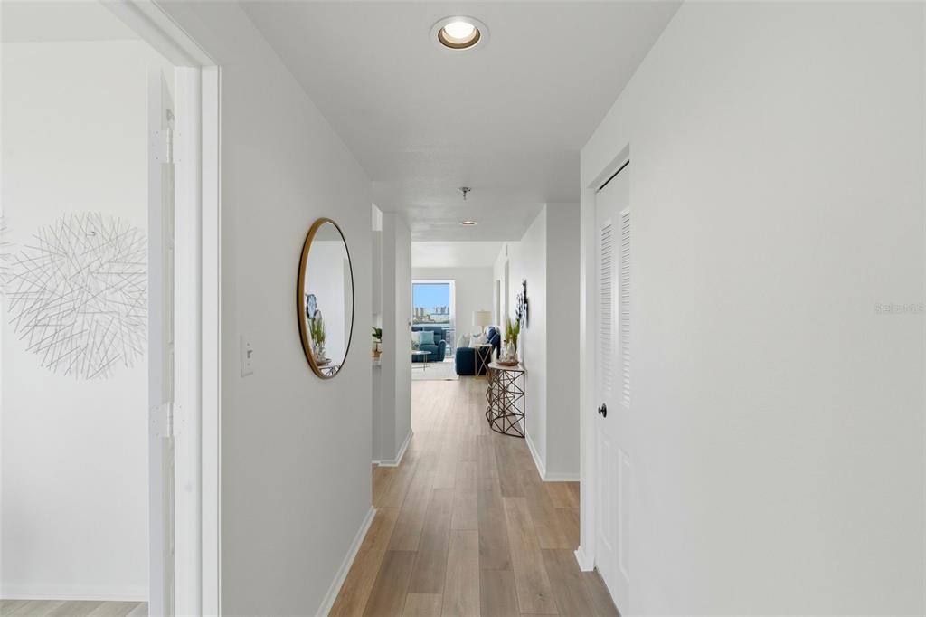 A hallway with light wood flooring leads to a living area with a balcony view — 7932 SAILBOAT KEY BOULEVARD S UNIT 701, SOUTH PASADENA, FL