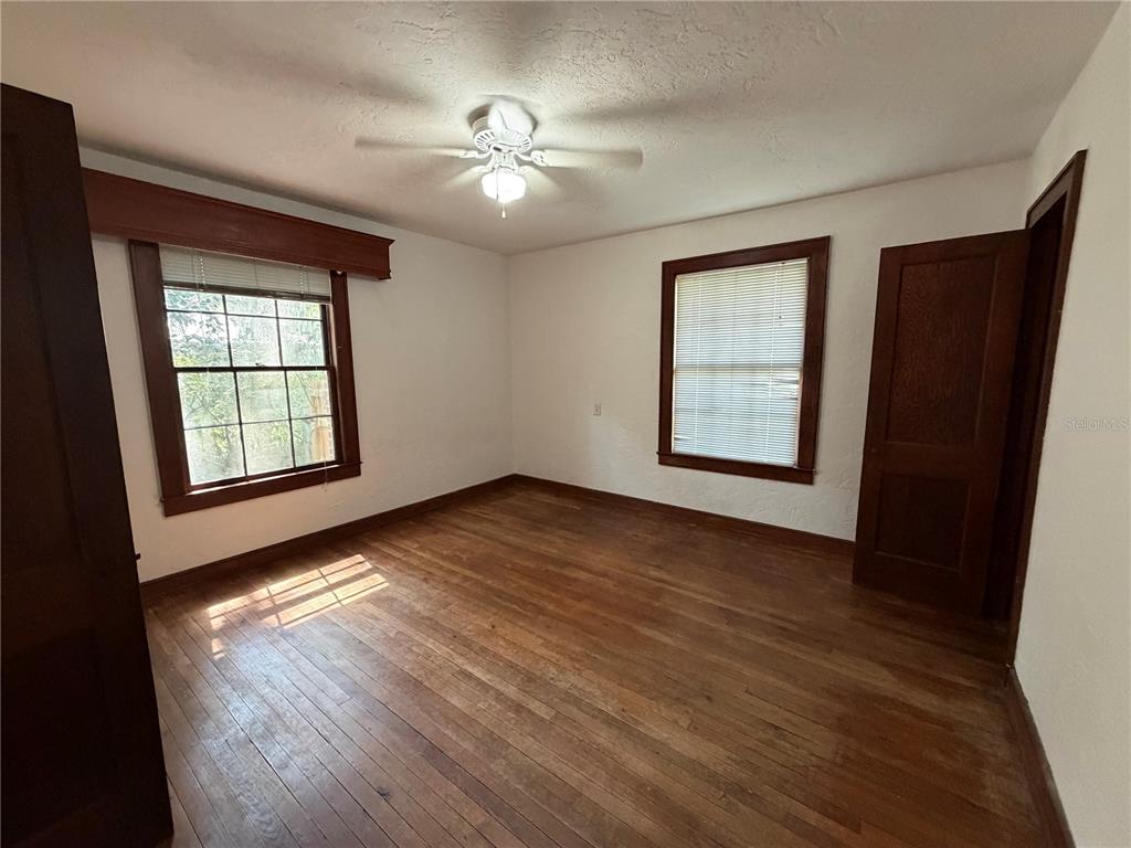 An empty bedroom features white walls, hardwood floors, a ceiling fan, and two windows — 1740 NW 7TH AVENUE, GAINESVILLE, FL