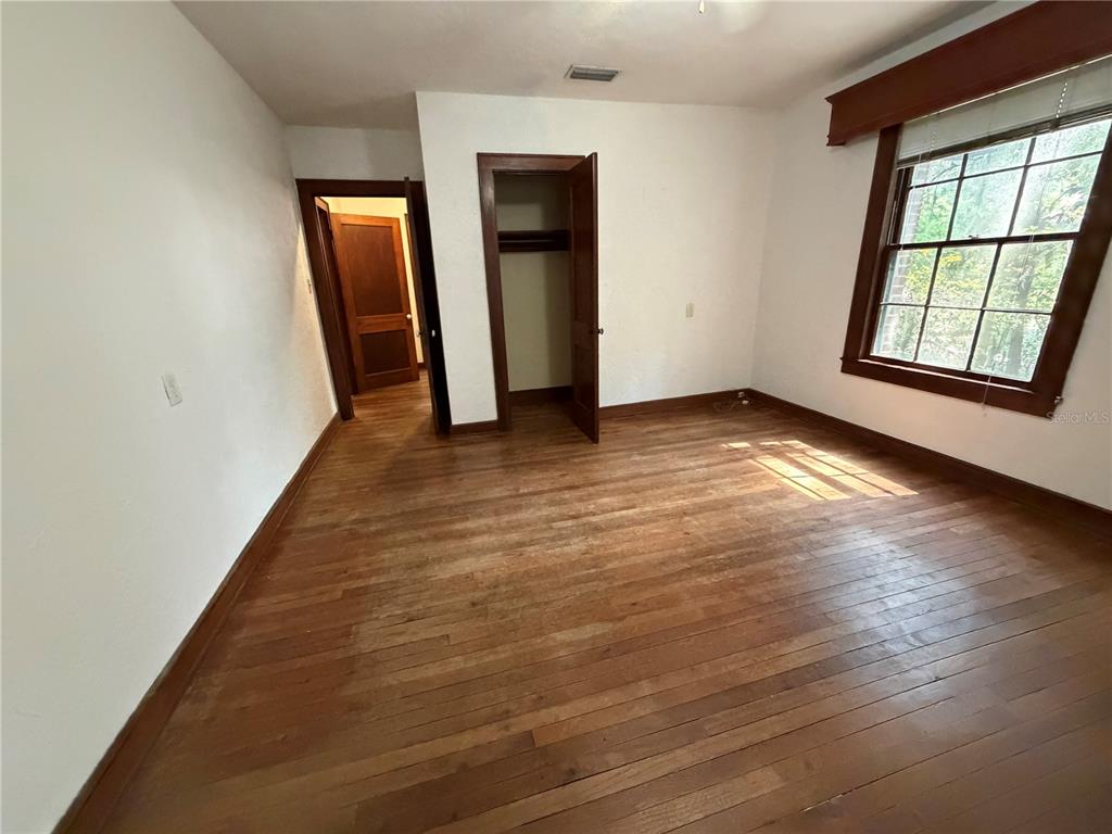 An empty bedroom features hardwood floors, a window with a valance, and two wooden doors — 1740 NW 7TH AVENUE, GAINESVILLE, FL
