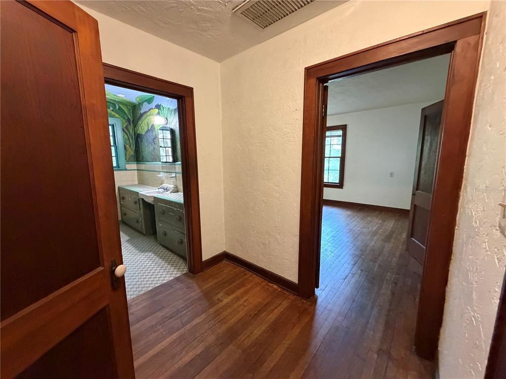A hallway with hardwood floors leads to a bathroom on the left and a bedroom — 1740 NW 7TH AVENUE, GAINESVILLE, FL